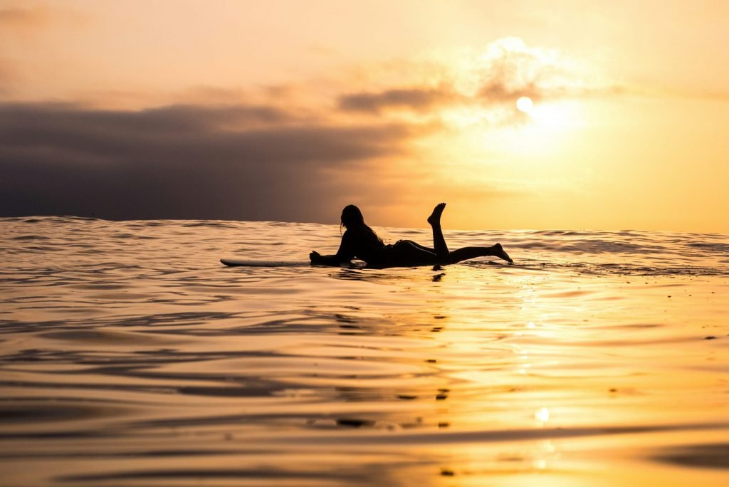Silhouette of a surfer lying prone on a surfboard on the ocean surface during a golden sunset.
